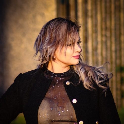 360piranha piranha network solutions piranha-usa Portrait of Dina W. confidently posing outdoors in golden-hour lighting, wearing a stylish black textured blazer with gold buttons over a sheer, sparkly top. Her voluminous, wavy blonde-highlighted hair cascades over her shoulder as she looks to the side, exuding elegance and poise. A branded watermark '@DinainBusiness' is displayed at the bottom right, emphasizing her professional identity.